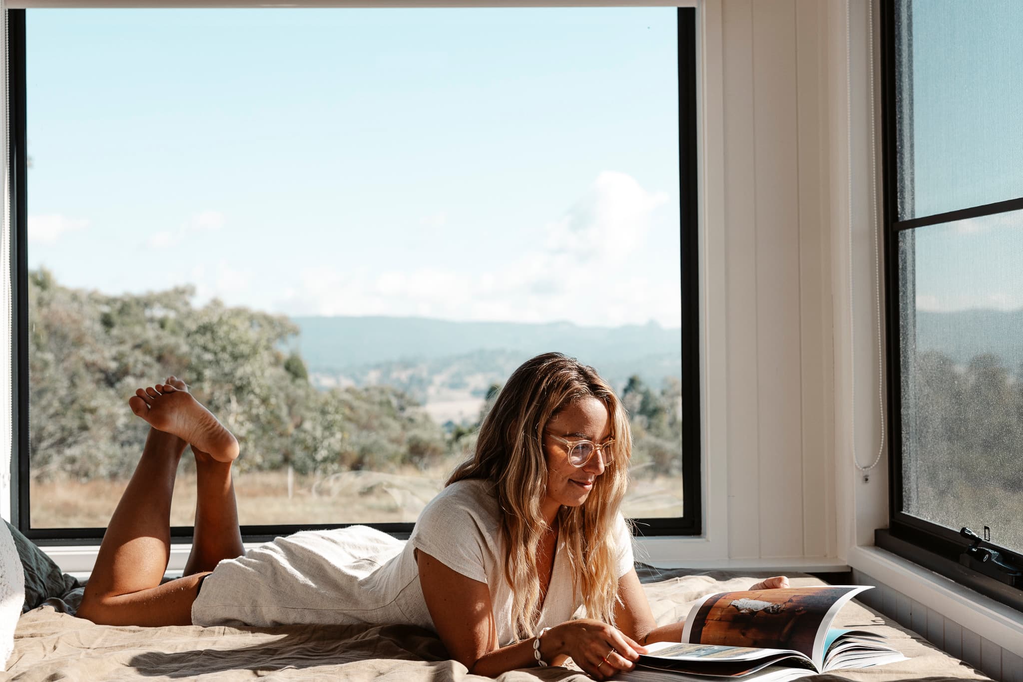 Woman reading on a bed with the view of Mudgee behind her.