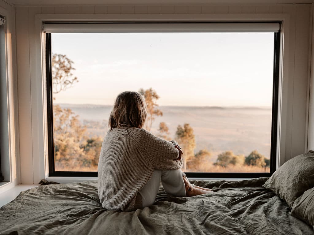 A woman relaxing in a tiny cabin surrounded by golden autumn leaves, enjoying a mindful seasonal reset in nature.